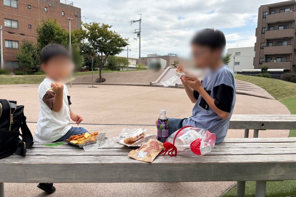 公園のベンチでおやつを食べる兄弟
